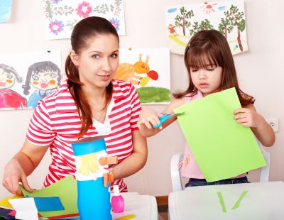 Kobieta wycina z kolorowego papieru z dzieckiem. Nauczycielka i dziewczynka w przedszkolu